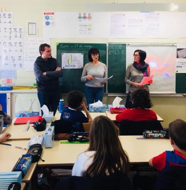 Trois professeurs (deux femmes, un homme) debout devant le tableau noir, dans une salle de classe